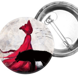 Könnte beinhalten: Eine rote, verhüllte Figur mit einem fließenden Umhang und einer schwarzen Wolfssilhouette vor einem weißen und grauen Hintergrund. Das Bild ist ein runder Knopf.