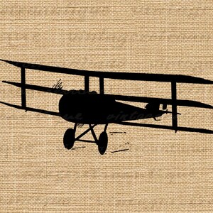 May include: Black silhouette of a vintage biplane aircraft with three wings. The plane is facing forward with the propeller visible. The plane is on a brown hessian background.