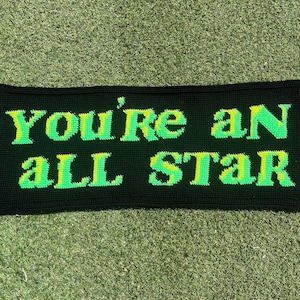 May include: A black crocheted banner with the text "You're an all star" in green and yellow yarn.