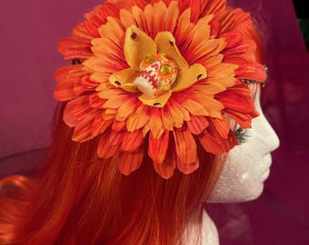 May include: A large orange flower with a smaller yellow flower in the center. The smaller flower has a white skull design.