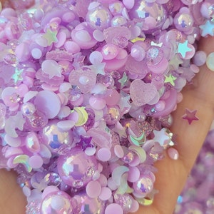 Könnte beinhalten: Eine Sammlung von violetten und schillernden Harzemblemen, darunter Sterne, Monde, Herzen und Perlen. Die Embleme sind perfekt, um Kunsthandwerk und Projekten einen Hauch von Glanz zu verleihen.
