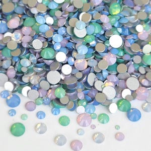 May include: A collection of small, round, flat-backed cabochons in various sizes and pastel colors, including light blue, mint green, and soft lavender. The pieces have a smooth, opaque finish and are scattered across a plain white surface.