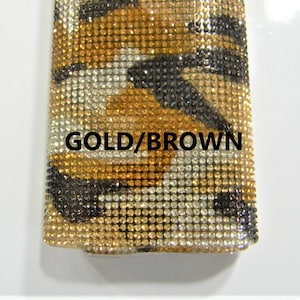 May include: A close-up of a gold and brown fabric with a rhinestone pattern. The fabric has a tiger print design. The text "GOLD/BROWN" is visible on the fabric.