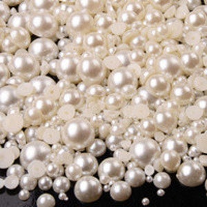 May include: A large assortment of white pearl beads in various sizes. The beads are scattered on a black surface.