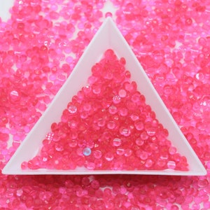 Puede incluir: Un plato triangular blanco lleno de piedras de cristal rosa iridiscentes. El plato está rodeado de más piedras de cristal rosa.
