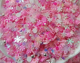 Pode incluir: Uma coleção de decorações para artesanato em tons de rosa e branco, apresentando pequenas formas de plástico, incluindo flocos de neve, balas de hortelã listradas, contas redondas e pequenas peças em formato de coração com acabamento brilhante.