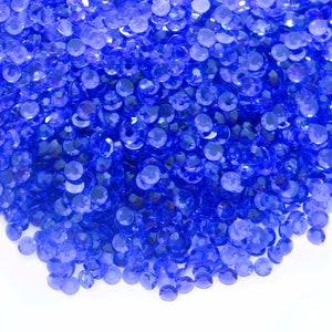 May include: A large pile of small, round, blue rhinestones. The rhinestones are scattered on a white background.