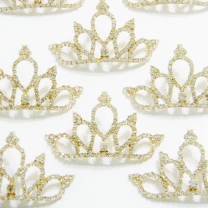 Pode incluir: Um conjunto de sete coroas douradas com detalhes de strass transparentes. As coroas são pequenas e delicadas, perfeitas para adicionar um toque de brilho a qualquer projeto.