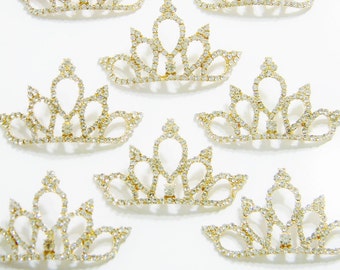 Pode incluir: Um conjunto de sete coroas douradas com detalhes de strass transparentes. As coroas são pequenas e delicadas, perfeitas para adicionar um toque de brilho a qualquer projeto.