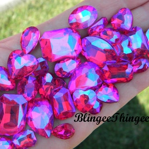 May include: Assortment of pink iridescent rhinestones in various shapes and sizes.  The rhinestones are arranged on a hand.  The text "BlinggeeThinggee" is visible in the lower right corner of the image.