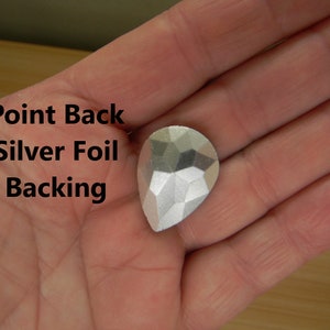 May include: A silver teardrop-shaped rhinestone with a pointed back and silver foil backing.  Point Back Silver Foil Backing.