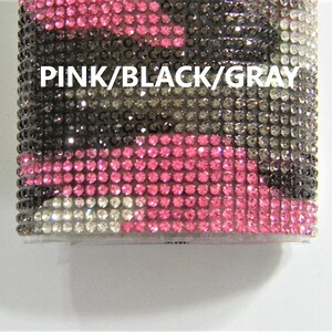 May include: A pink, black, and gray camouflage pattern phone case covered in rhinestones. The text "PINK/BLACK/GRAY" is printed on the case.