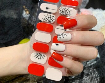 May include: A sheet of Halloween-themed nail wraps featuring a mix of red, white, and black designs. The wraps include solid red, solid white, spiderwebs, and spiders. The image also shows a hand with nails painted in matching designs.
