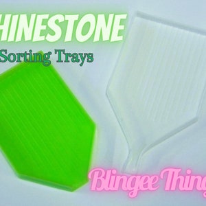 May include: Two diamond-shaped rhinestone sorting trays. One tray is green and the other is clear. The trays have lines to help sort the rhinestones. The text "Rhinestone Sorting Trays" is at the top of the image. The text "Blinghee Thinghee" is at the bottom of the image.