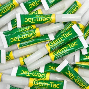 May include: A collection of small tubes of Gem-Tac permanent glue for rhinestones, gems, and more. Each tube is green and yellow with white caps, clearly labeled with the brand name Gem-Tac and a volume of .17 fl oz (5ml) per individual unit.