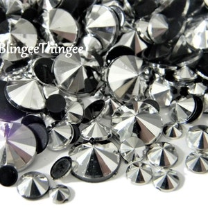 May include: A collection of sparkling, faceted rhinestones in various sizes and shapes. The rhinestones are primarily silver and clear, with some black, creating a contrast. The image is a close-up, showing the reflective surfaces of the gems. The text "BlingeeThingee" is visible.