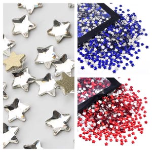 May include: An assortment of star-shaped rhinestones in various colors. Some are clear, some are gold glitter, and others are red and blue, likely for patriotic crafts. The rhinestones are scattered on a light gray surface.