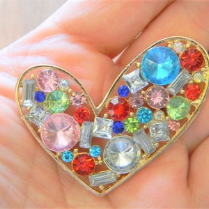 May include: A gold heart-shaped brooch with a variety of colorful rhinestones, including pink, blue, green, red, and clear.