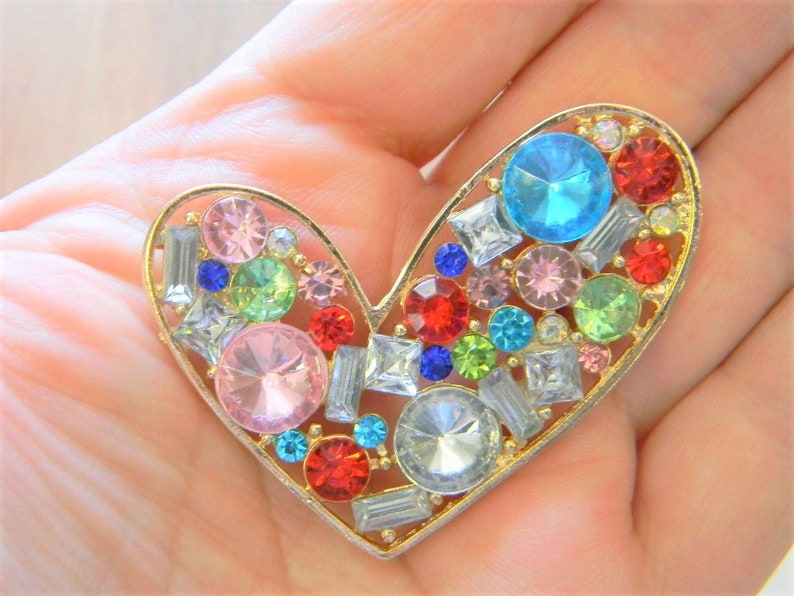 May include: A gold heart-shaped brooch with a variety of colorful rhinestones, including pink, blue, green, red, and clear.