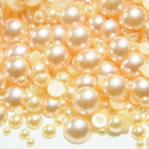 May include: A collection of pearl-like embellishments in various sizes, ranging from small to large, with a soft, creamy white color. The embellishments are scattered on a white surface.