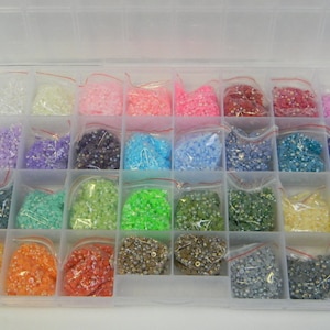 May include: A clear plastic storage box filled with small, colorful beads. The beads are organized in rows and columns, with each compartment containing a different color.