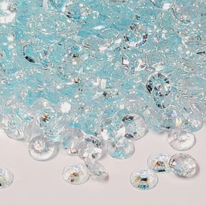 May include: A pile of light blue iridescent rhinestones, with a few scattered on a white surface.