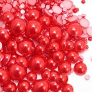 May include: A large assortment of red pearl beads in various sizes. The beads are shiny and have a smooth, round shape.