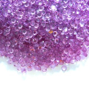 May include: A large pile of small, round, purple gemstones. The gemstones are scattered on a white surface.