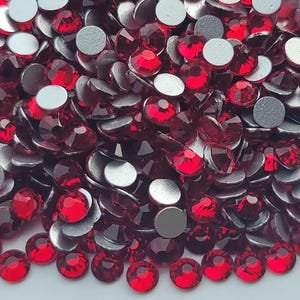 May include: A close-up of a pile of red rhinestones with silver backs. The rhinestones are small and round, and they are arranged in a random pattern.