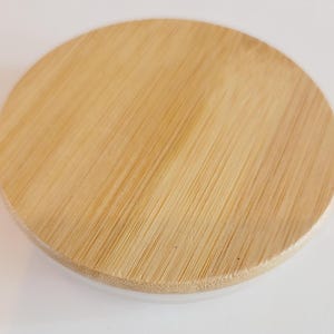 May include: A round, natural wood lid with a smooth, light brown finish. The lid is made of bamboo and has a slightly raised edge.