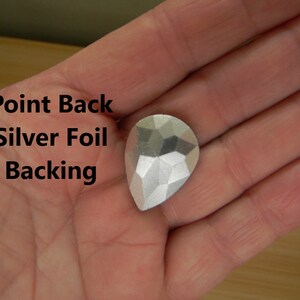 May include: A silver teardrop-shaped rhinestone with a pointed back and silver foil backing.  Point Back Silver Foil Backing.