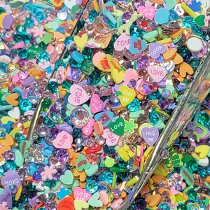 May include: A scoop of colorful heart-shaped sprinkles with various words and phrases like "Love", "XOXO", "Cutie Pie", and "Hug Me".