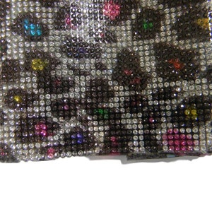 May include: A close-up of a black and white fabric covered in small, colorful rhinestones. The rhinestones are arranged in a pattern that resembles a leopard print.
