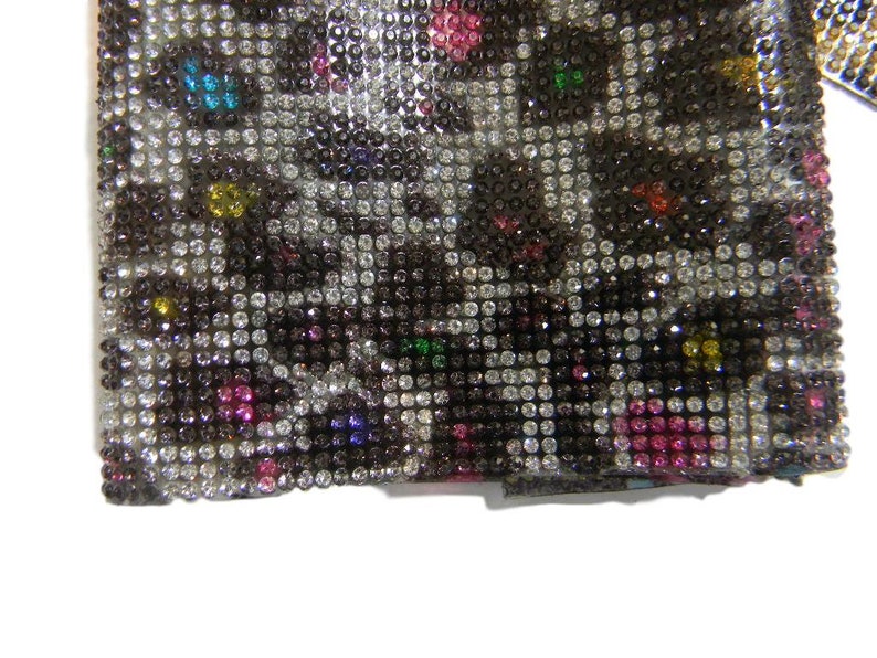 May include: A close-up of a black and white fabric covered in small, colorful rhinestones. The rhinestones are arranged in a pattern that resembles a leopard print.