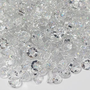 May include: A pile of clear iridescent rhinestones, scattered on a white surface.