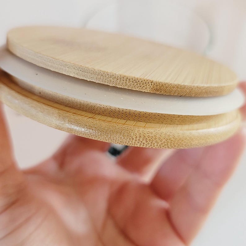 May include: A close-up of a round, wooden lid with a white silicone seal. The lid is made of light brown bamboo and has a smooth, polished finish.