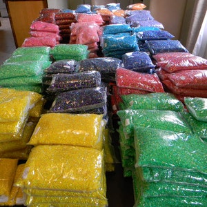 May include: A large collection of colorful iridescent beads packaged in clear plastic bags. The beads are arranged in rows by color, with each row containing multiple bags.