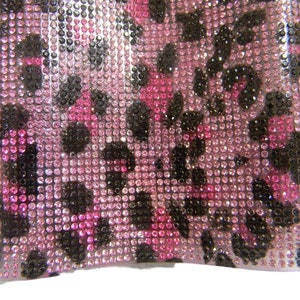 May include: Pink and black leopard print fabric covered in small, clear rhinestones.