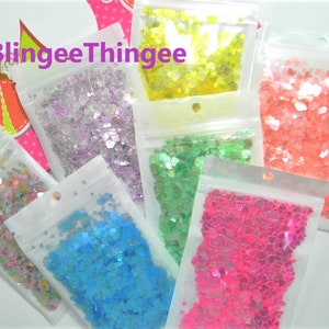 May include: Assortment of iridescent heart-shaped glitter in various colors, including pink, green, blue, yellow, and purple, packaged in clear plastic bags with a hole at the top.