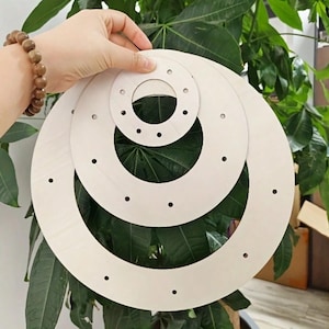 May include: Three nested circular wooden frames of varying sizes, each featuring evenly spaced small holes along the perimeter. The light-colored, smooth wooden rings are stacked concentrically, showcasing a simple, flat, and unfinished design.