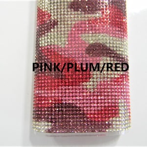 May include: A close-up of a pink, plum, and red rhinestone-covered phone case. The case is made of a clear material with a textured surface. The rhinestones are arranged in a pattern that resembles camouflage.