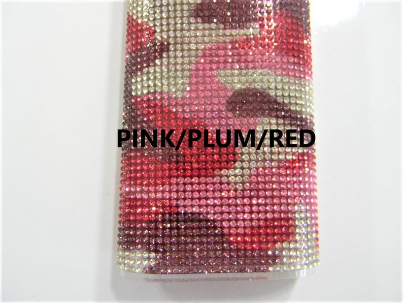 May include: A close-up of a pink, plum, and red rhinestone-covered phone case. The case is made of a clear material with a textured surface. The rhinestones are arranged in a pattern that resembles camouflage.
