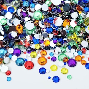 May include: A collection of colorful, sparkling rhinestones in various sizes and shades, including red, blue, yellow, green, orange, and purple. Some rhinestones have a mirrored backing, creating a dazzling effect. The scattered arrangement creates a vibrant, eye-catching display.