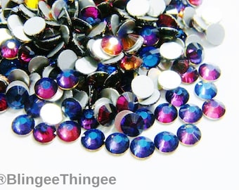 May include: Assortment of iridescent blue and purple rhinestones with silver backing. The rhinestones are scattered on a white surface.