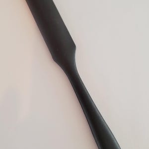May include: A black plastic spatula with a rounded handle and a hole at the end.