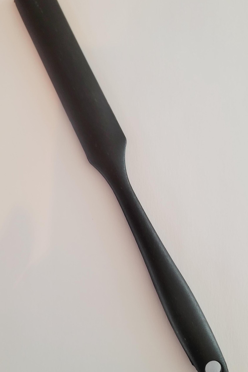 May include: A black plastic spatula with a rounded handle and a hole at the end.