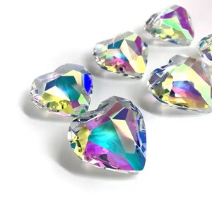 May include: A group of six iridescent heart-shaped crystal prisms. The prisms are clear with a rainbow effect.