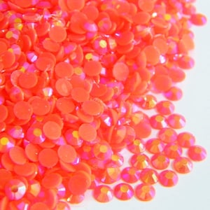 May include: A pile of bright orange iridescent rhinestones. The rhinestones are small and round, and they have a shiny, reflective surface.