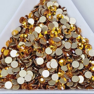 May include: A pile of small, round, gold-colored rhinestones with flat backs. The rhinestones are arranged in a triangular shape.