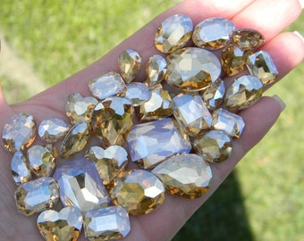 May include: A collection of faceted glass rhinestones in various shapes and sizes. The rhinestones are a light amber color with a clear, iridescent finish.